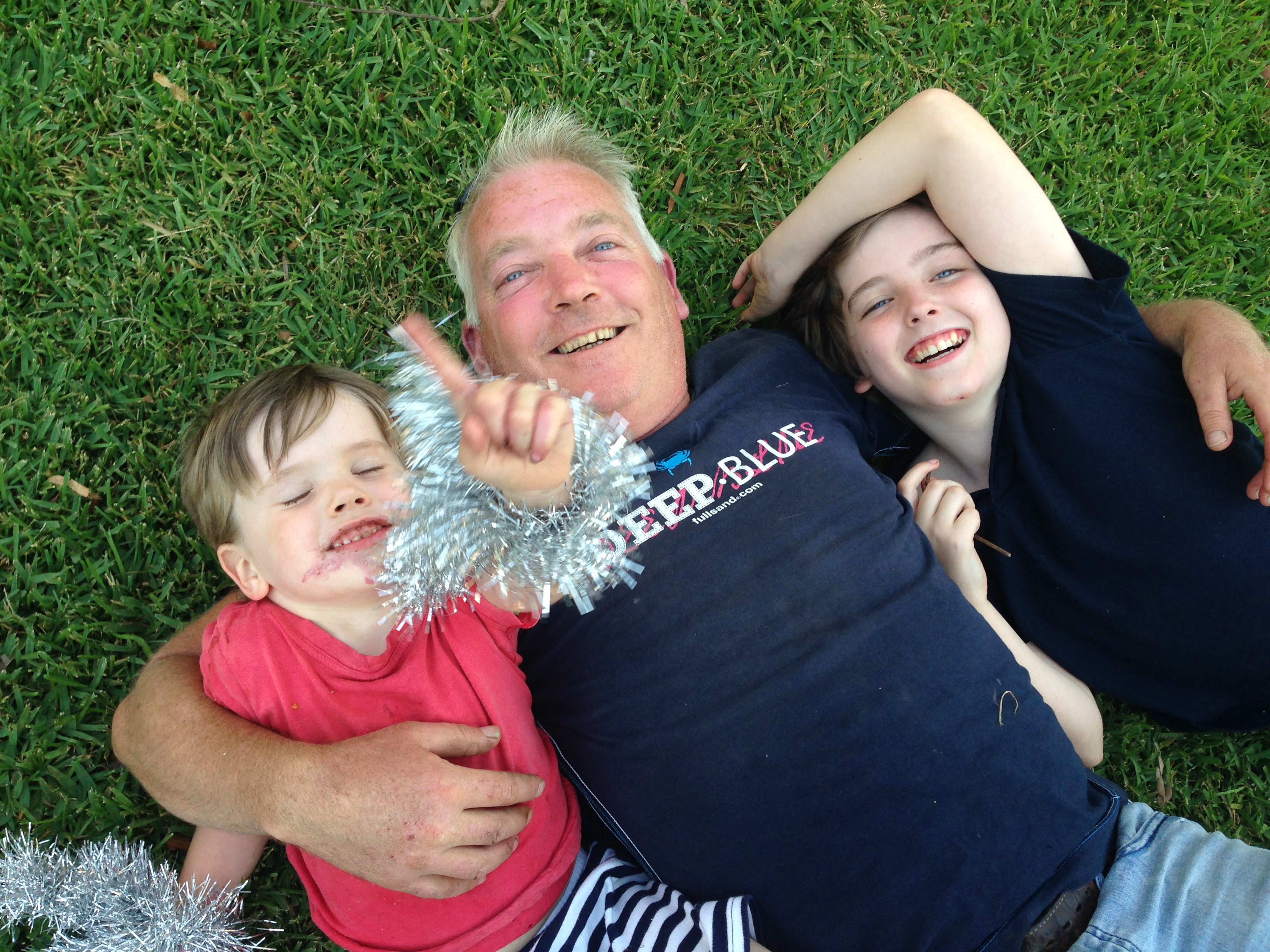 David lying on the grass with his two young sons, Christmas tinsel in hand